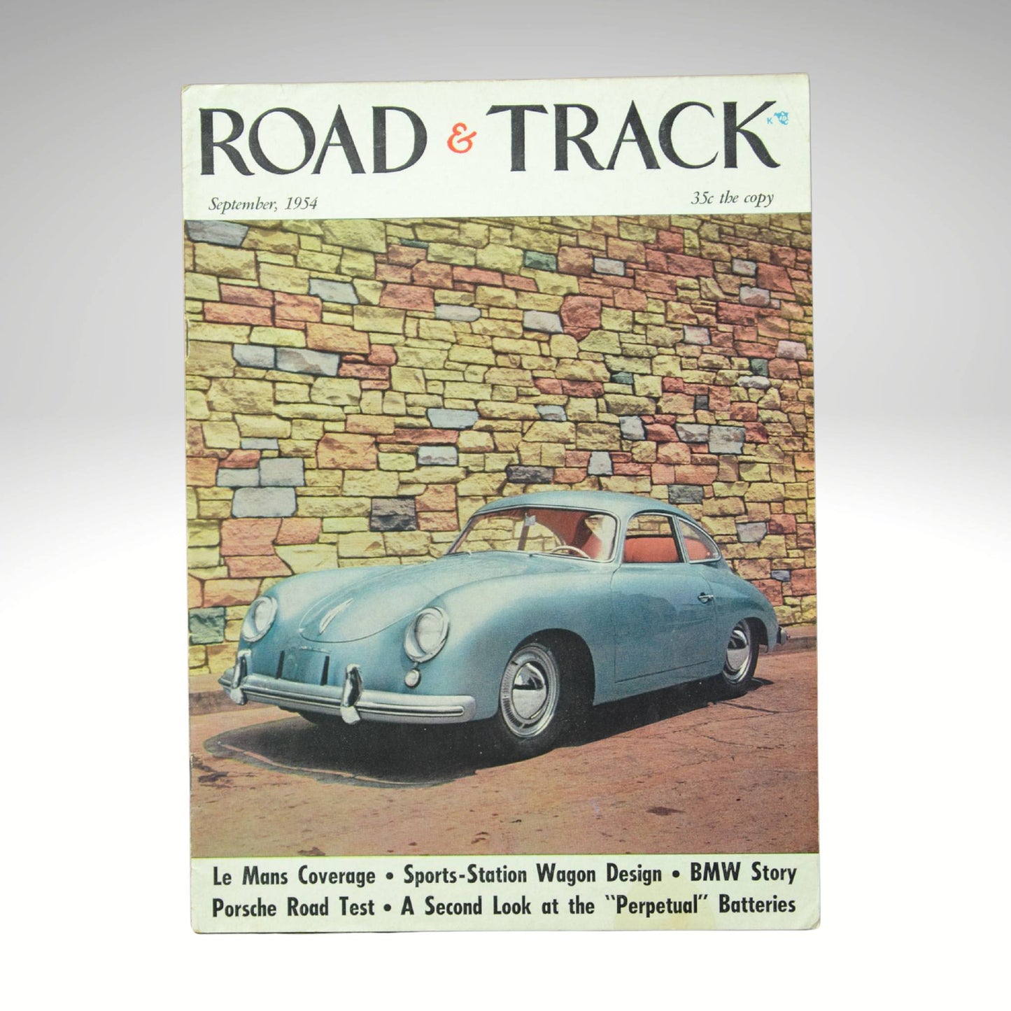 Vintage 'Road & Track' magazine cover with a blue Porsche car against a stone wall.