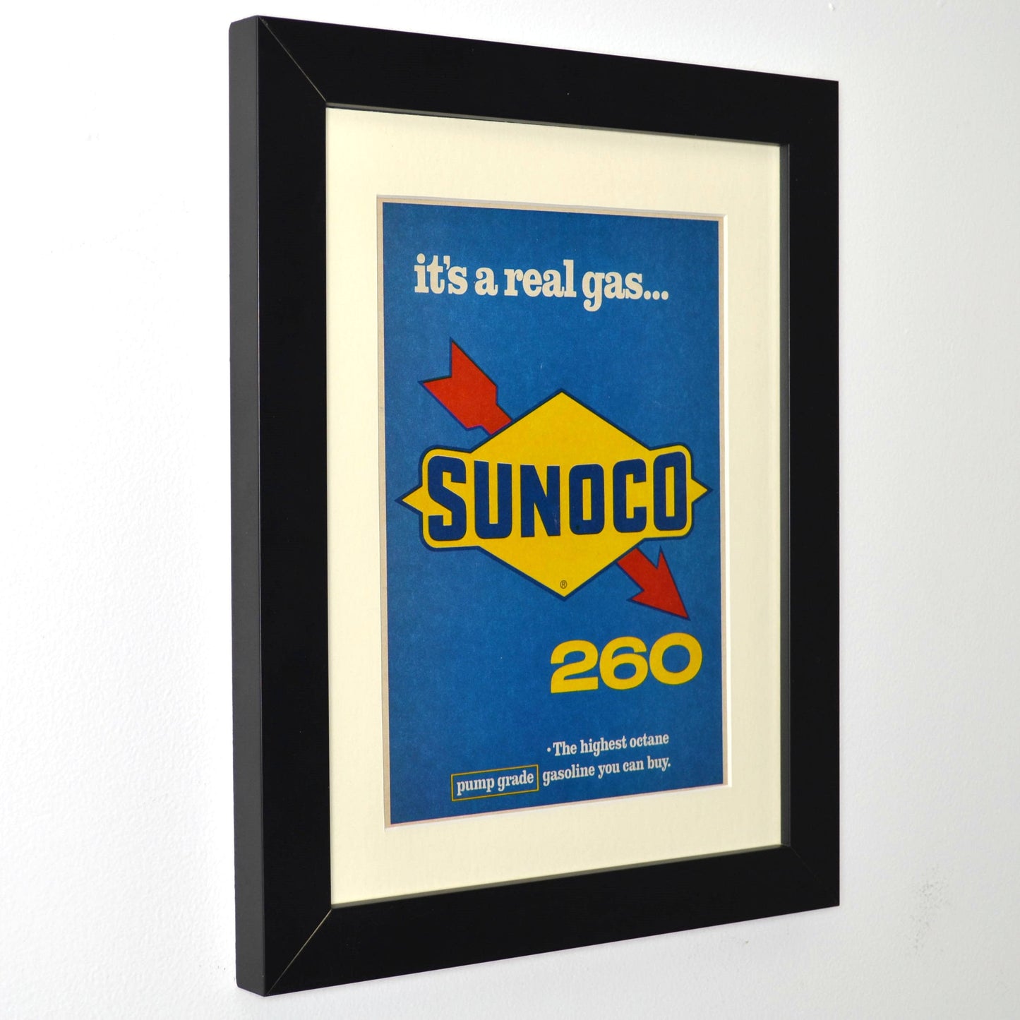 Framed vintage 1966 Sunoco 260 print ad featuring the bold blue and yellow Sunoco logo and the tagline ‘It’s a real gas...’ Professionally dry mounted and displayed in a 10x13 matte black frame with white matting side view