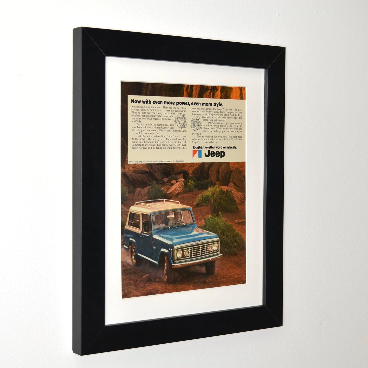 Framed side view of 1972 Jeep Commando print ad featuring a blue Jeep navigating rugged terrain. A perfect piece of retro automotive wall art for Jeep enthusiasts.