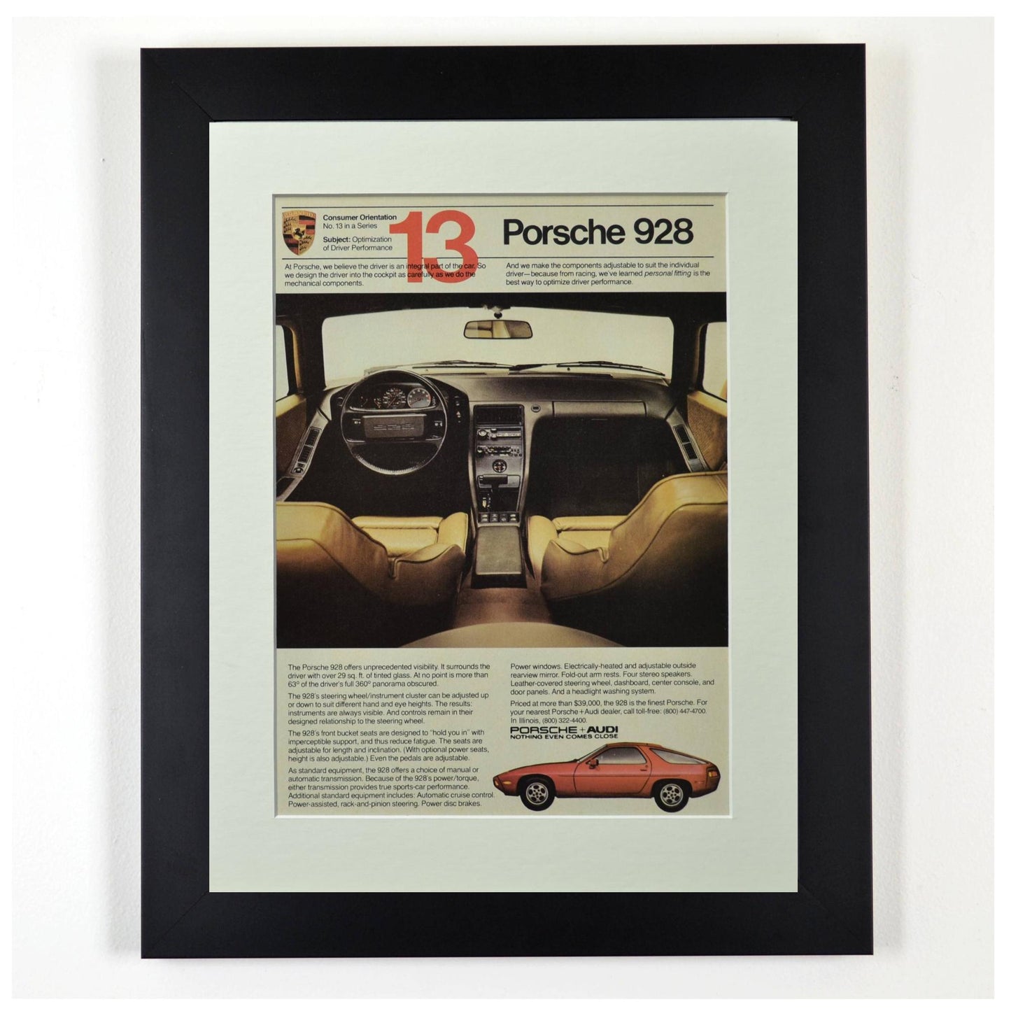 Framed vintage 1980 Porsche 928 ad showing interior cockpit view and orange 928 side profile, dry-mounted and matted in black frame.
