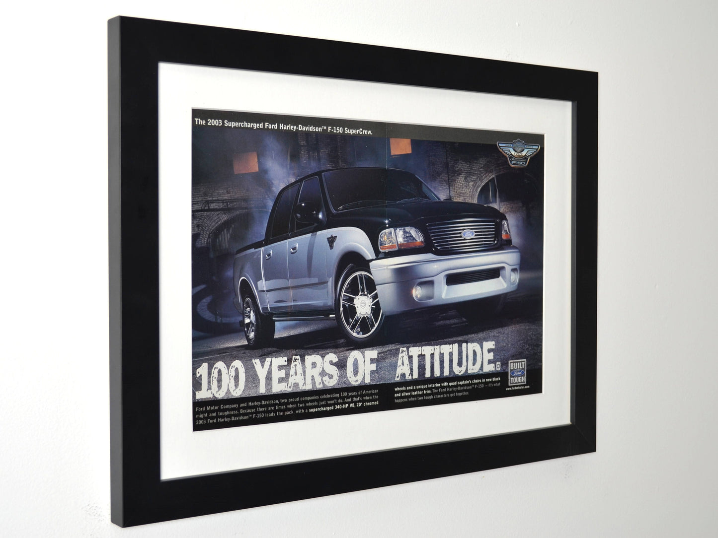 Framed vintage 2003 Ford Harley-Davidson F-150 print ad featuring a black and silver SuperCrew pickup with Harley-Davidson badging. Professionally dry mounted and displayed in a 15x20 matte black frame with white matting side view