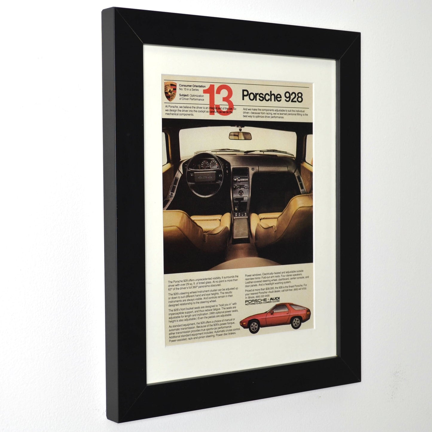Framed vintage 1980 Porsche 928 ad showing interior cockpit view and orange 928 side profile, dry-mounted and matted in black frame side view