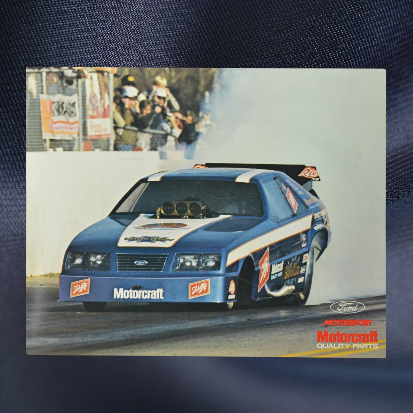 1983 NHRA hero card showing Raymond Beadle’s Blue Max Mustang Funny Car in action, burning rubber down the dragstrip with a crowd in the background.