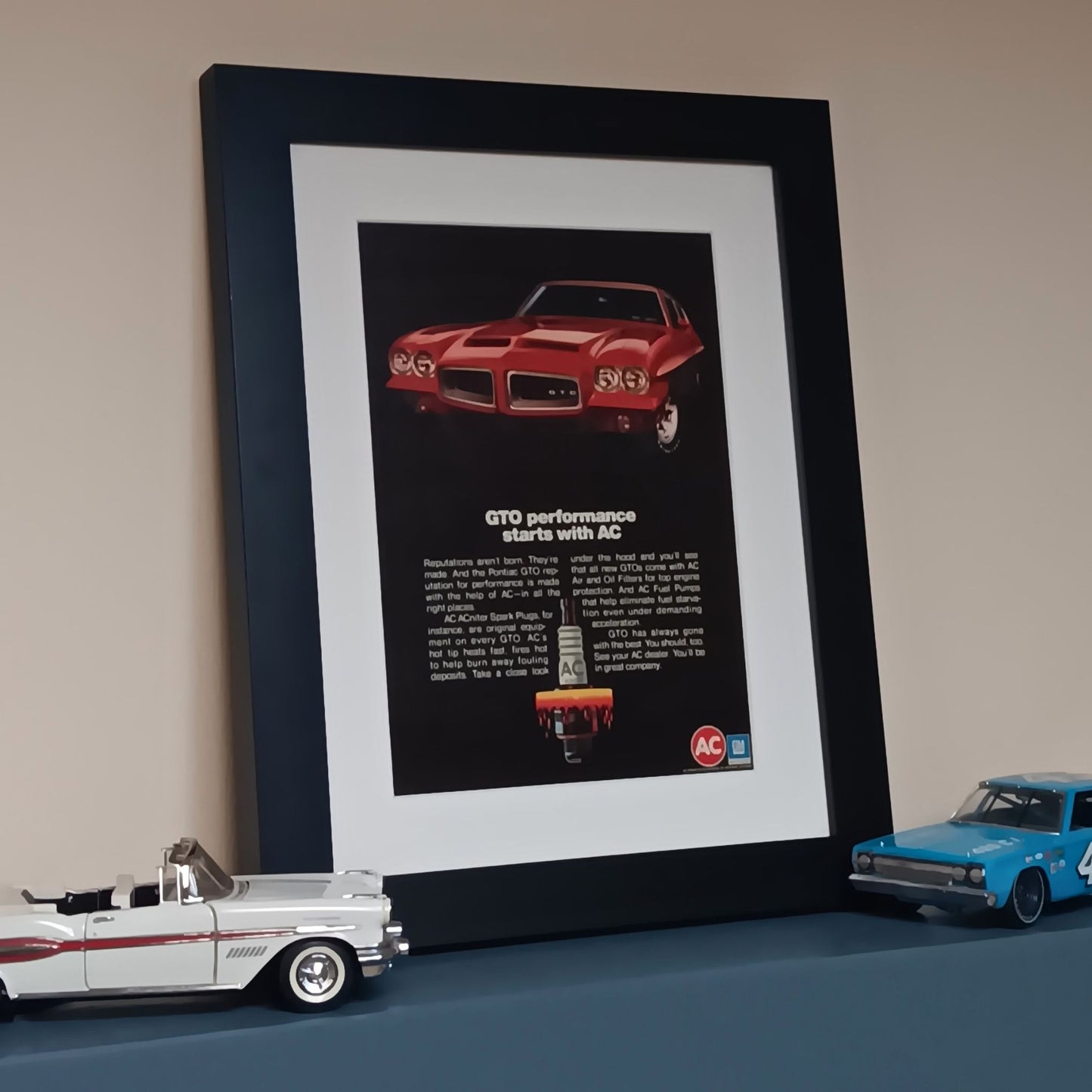 Framed advertisement for a red muscle car with text and AC logo, vintage art garage