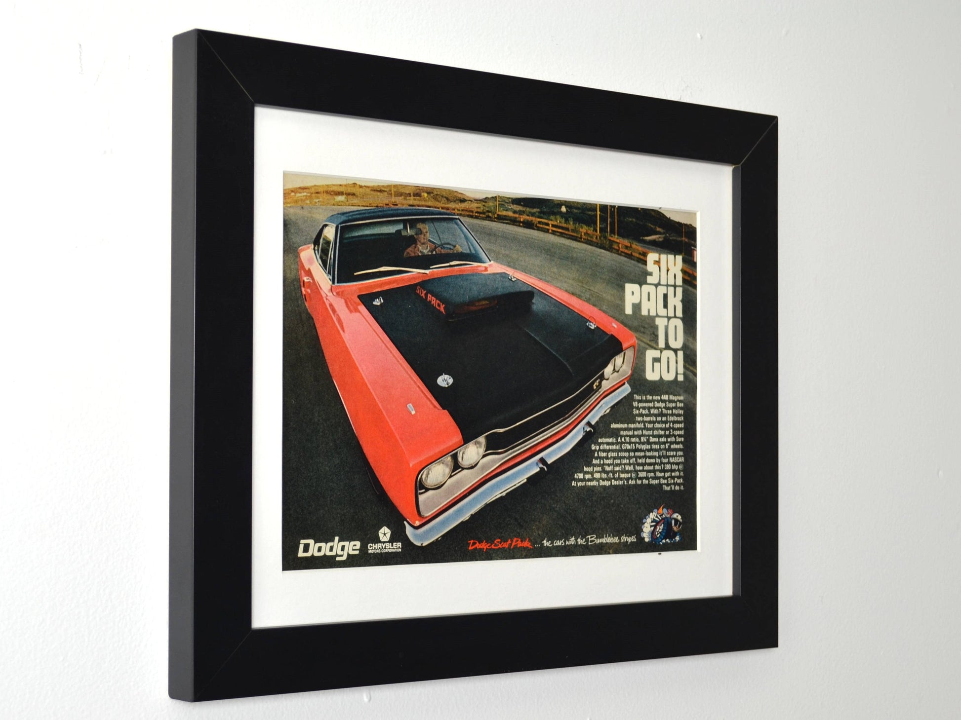 Framed 1970 Dodge Super Bee 440 Six Pack vintage print ad featuring an orange Super Bee with matte black Six Pack hood and “Six Pack to Go!” slogan — authentic Mopar wall art for collectors and enthusiasts side view