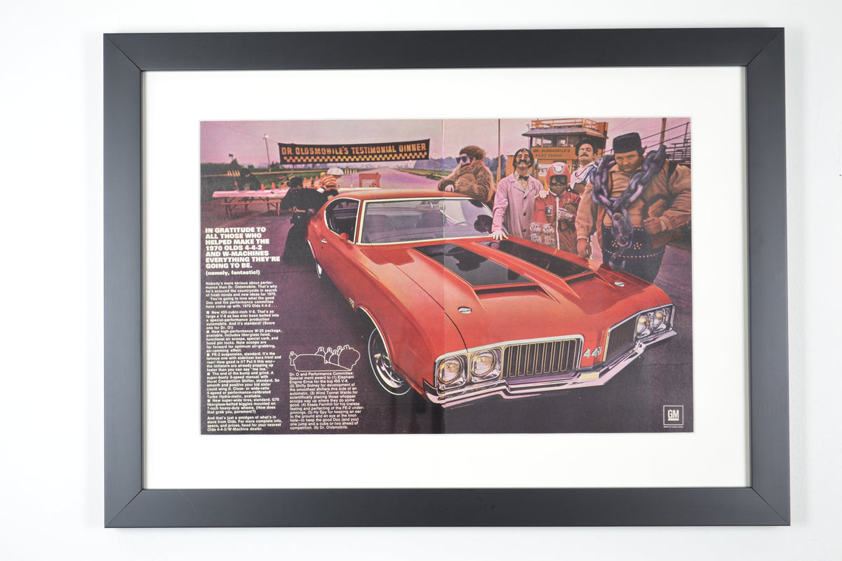 Framed vintage 1970 Oldsmobile 442 advertisement featuring a bright red muscle car at a trackside testimonial dinner. A must-have for classic car collectors