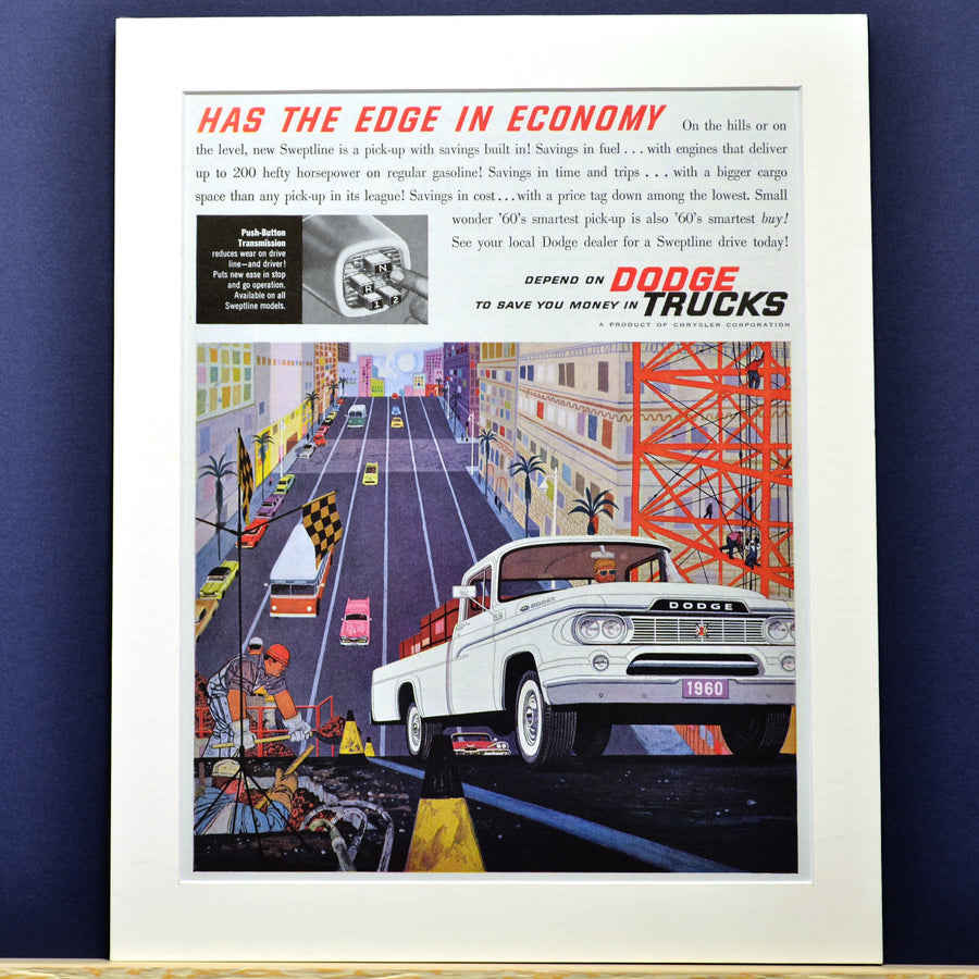 Vintage advertisement for Dodge trucks with a white truck on a city street, framed against a blue wall.
