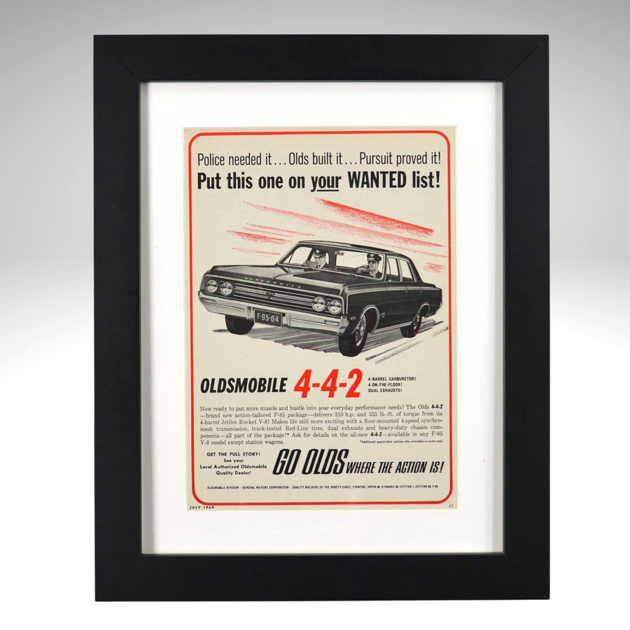 Framed 1964 Oldsmobile 442 print ad – black sedan with “Put this one on your WANTED list” headline, vintage muscle artwork.

