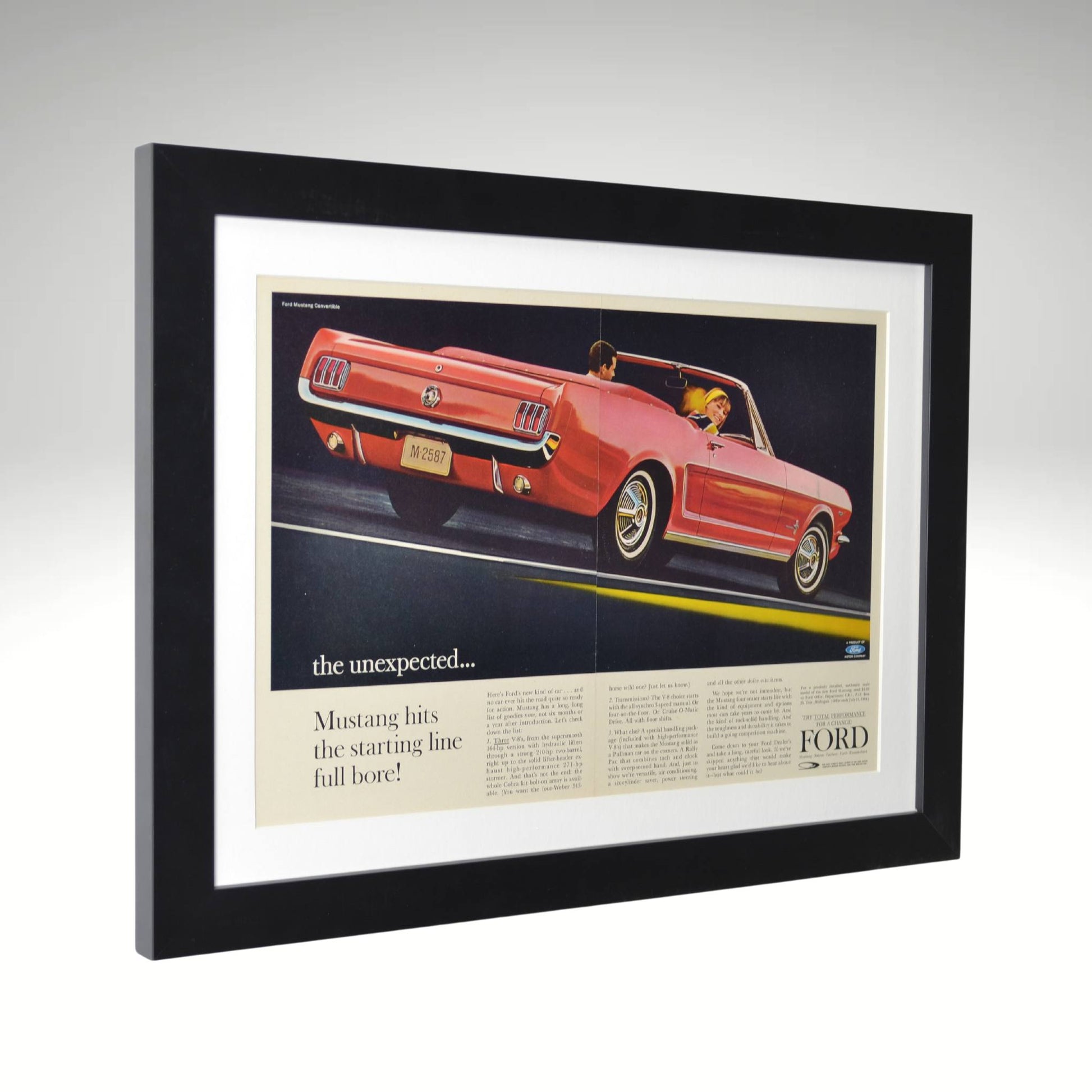 Side view of Framed 1964 Ford Mustang convertible print ad showcasing a red Mustang driving with passengers, beautifully framed with a black wood frame and white mat.