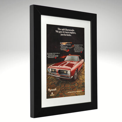 A framed vintage Plymouth Barracuda car advertisement print, shown at a three-quarter angle against a light gray gradient background. The print features a red muscle car on a cracked ground with white text above, set inside a white mat and a thick black frame.