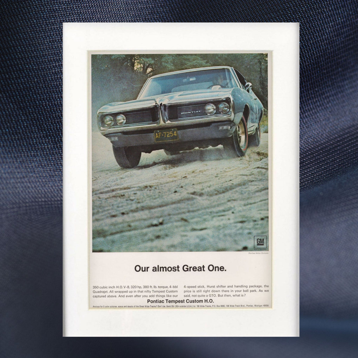 A vintage-style automotive poster print featuring a 1968 pontiac tempest car driving on a dirt road, with the headline 'Our almost Great One.' and small text below, displayed against a dark blue textured fabric background.