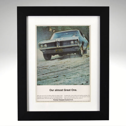 A framed vintage car advertisement print featuring a blue 1968 Pontiac tempest muscle car on a dirt road, with the headline 'Our almost Great One.' and smaller text below, shown in a black frame against a light gray background.
