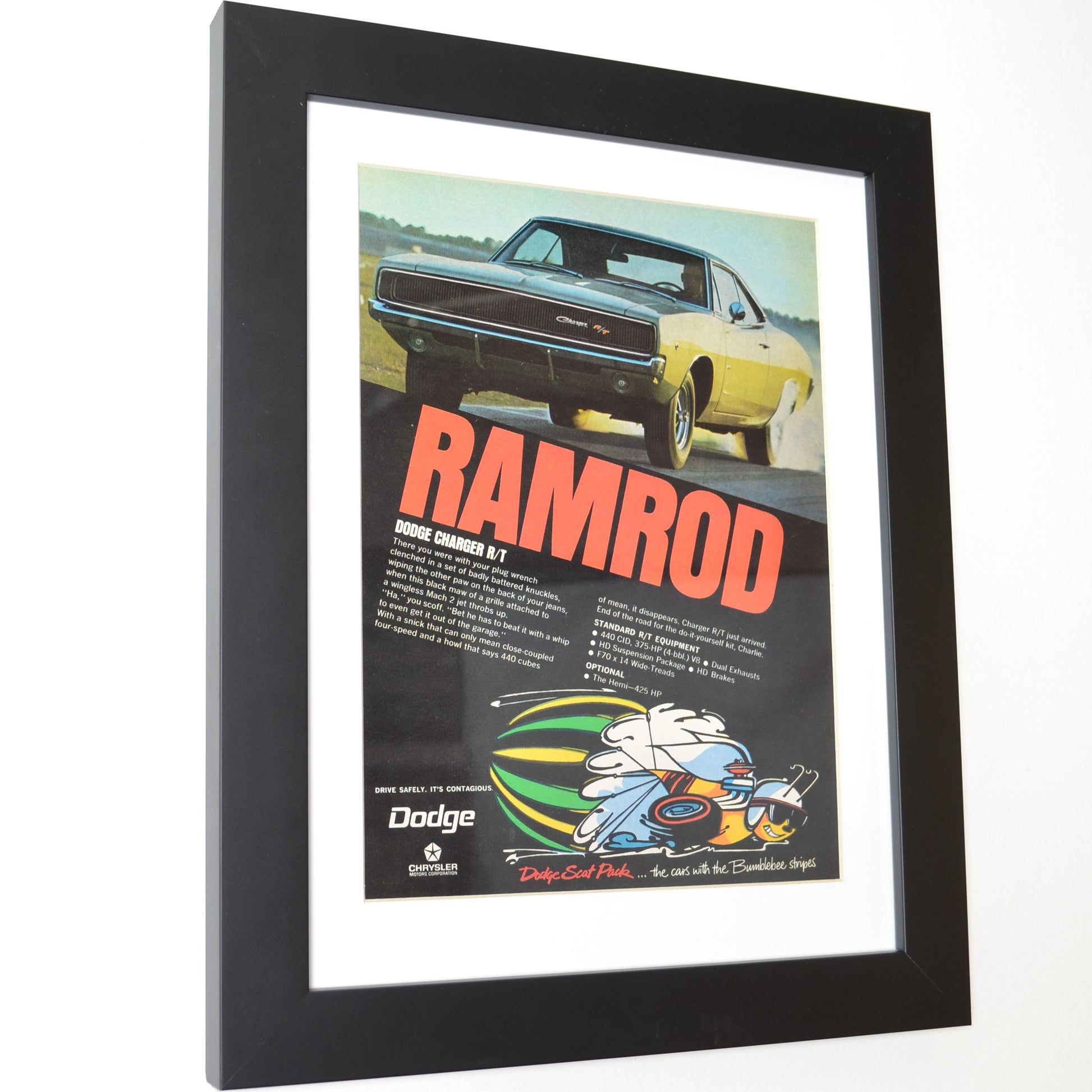 Framed 1969 Dodge Charger R/T “Ramrod” vintage print ad featuring a yellow Charger R/T launching hard with Scat Pack bumblebee logo and bold red lettering — authentic Mopar wall art for collectors side view