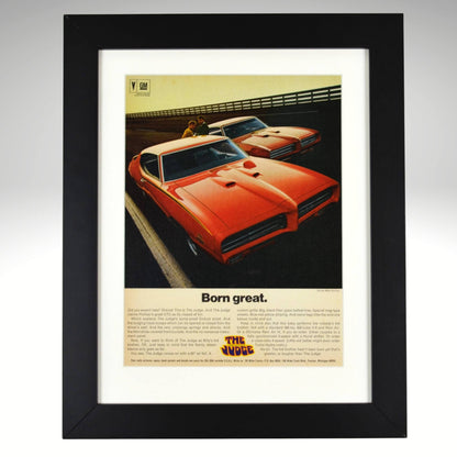 Framed 1969 Pontiac GTO Judge vintage print ad featuring two Carousel Red GTOs with headline “Born Great.” Displayed in a matte black frame with white mat — classic muscle car wall art for collectors and enthusiasts.