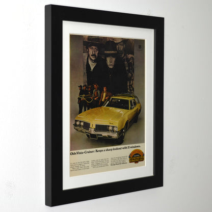Framed advertisement for Olds Vista-Cruiser with a yellow car and people in cowboy hats.