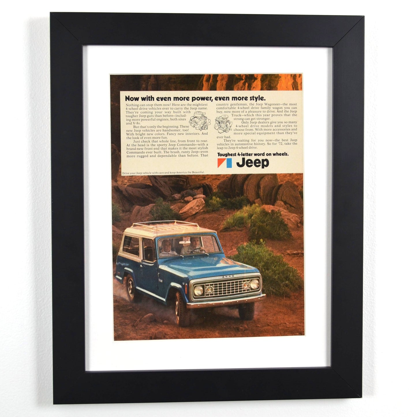 Framed 1972 Jeep Commando print ad featuring a blue Jeep navigating rugged terrain. A perfect piece of retro automotive wall art for Jeep enthusiasts.