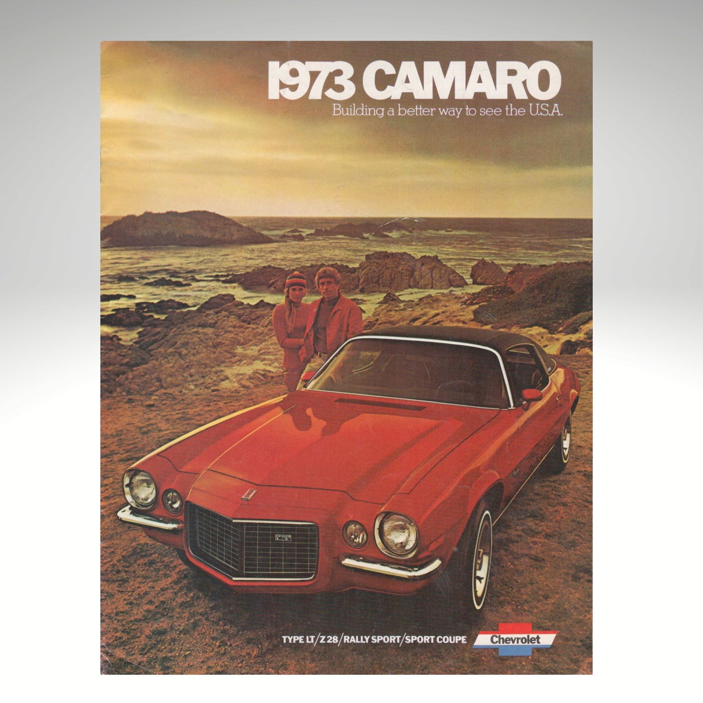 1973 Camaro advertisement with two people standing next to a red car in a scenic setting.
