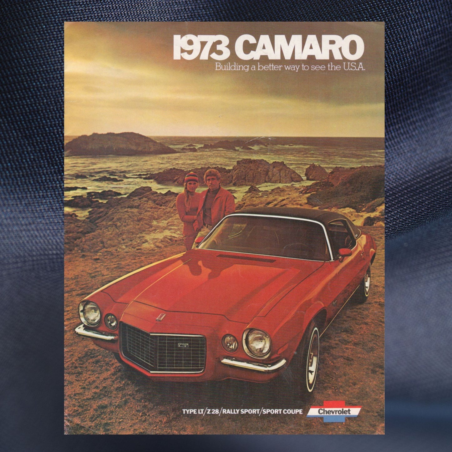 1973 Camaro advertisement with two people by a red car on a coastal landscape.