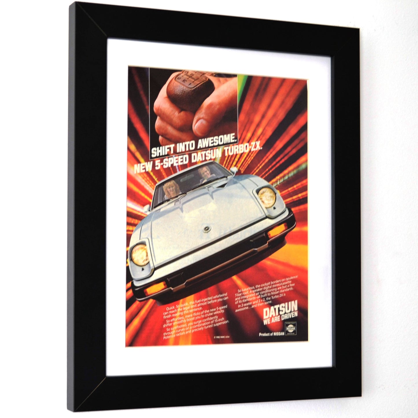 Framed 1982-datsun-280zx-turbo advertisement with a car and hand shifting gears on a white background