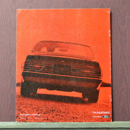 Vintage Ford Thunderbird brochure with red cover and black car illustration on a wooden surface