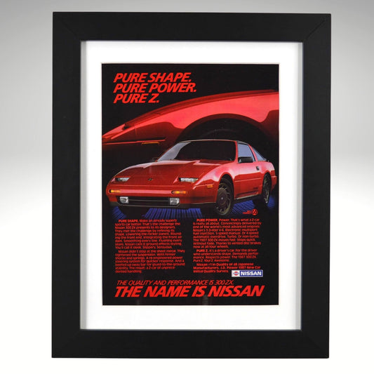 Framed 1987 Nissan 300ZX vintage print ad featuring a red 300ZX with bold headline “Pure Shape. Pure Power. Pure Z.” Displayed in a matte black frame with white mat — perfect retro automotive wall art for collectors.
