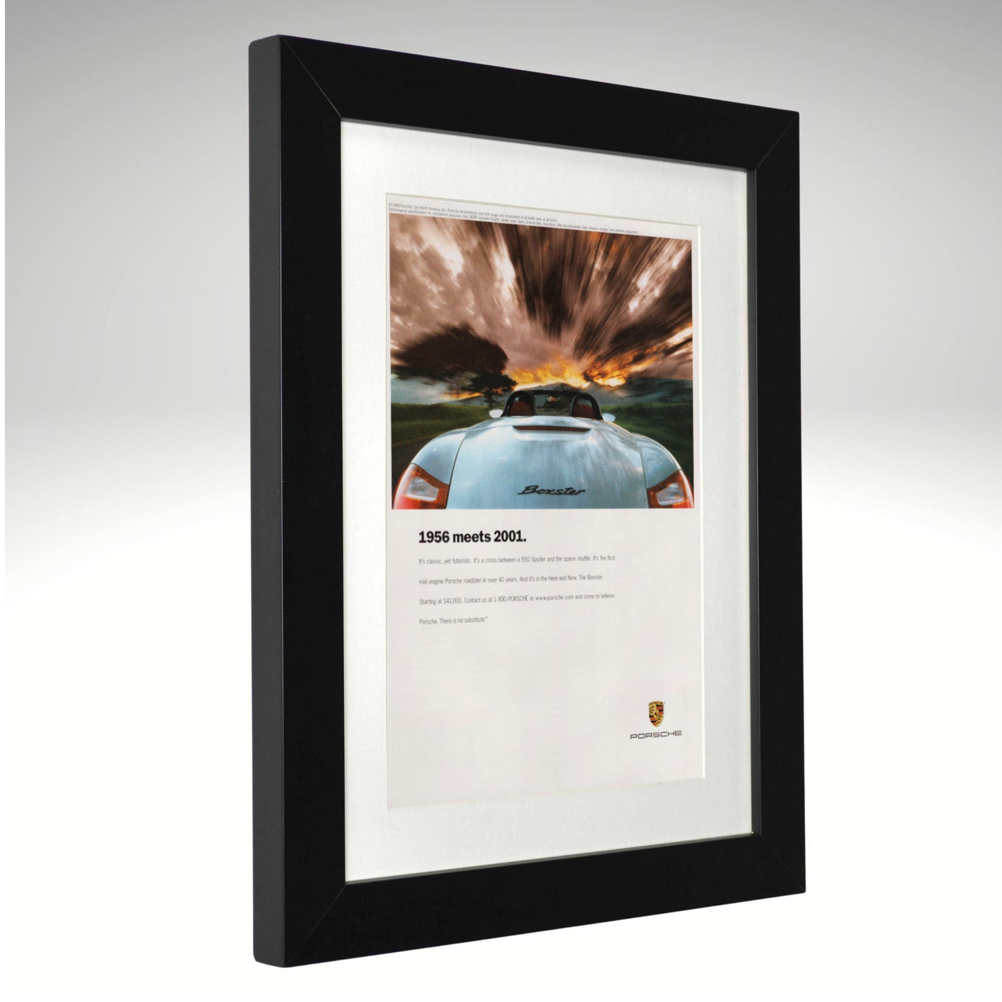 A framed Porsche print featuring a rear view photograph of a light blue Porsche 911 with dramatic storm clouds and a sunset, mounted in a black frame with a white mat on a light gray background.