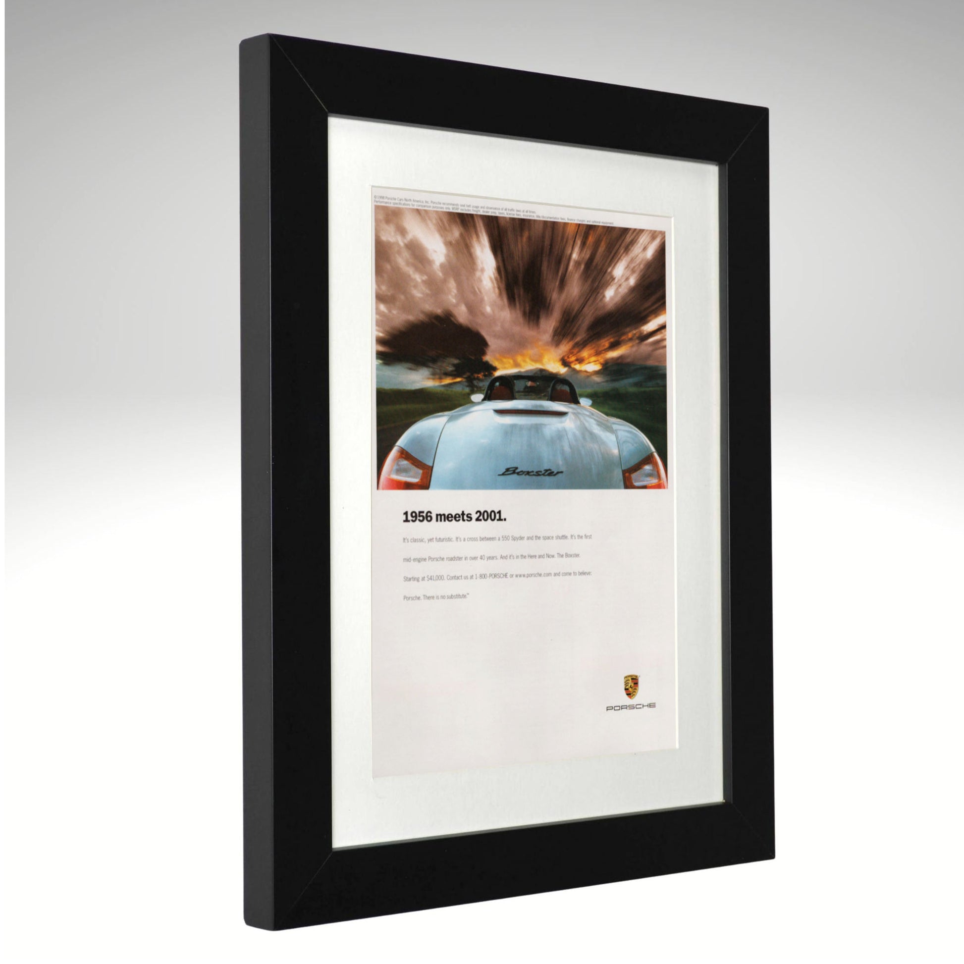 A framed Porsche print featuring a rear view photograph of a light blue Porsche 911 with dramatic storm clouds and a sunset, mounted in a black frame with a white mat on a light gray background.