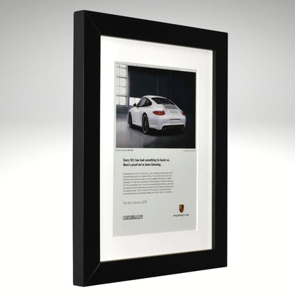 Framed advertisement of a white Porsche 911 GTS car on a gray background