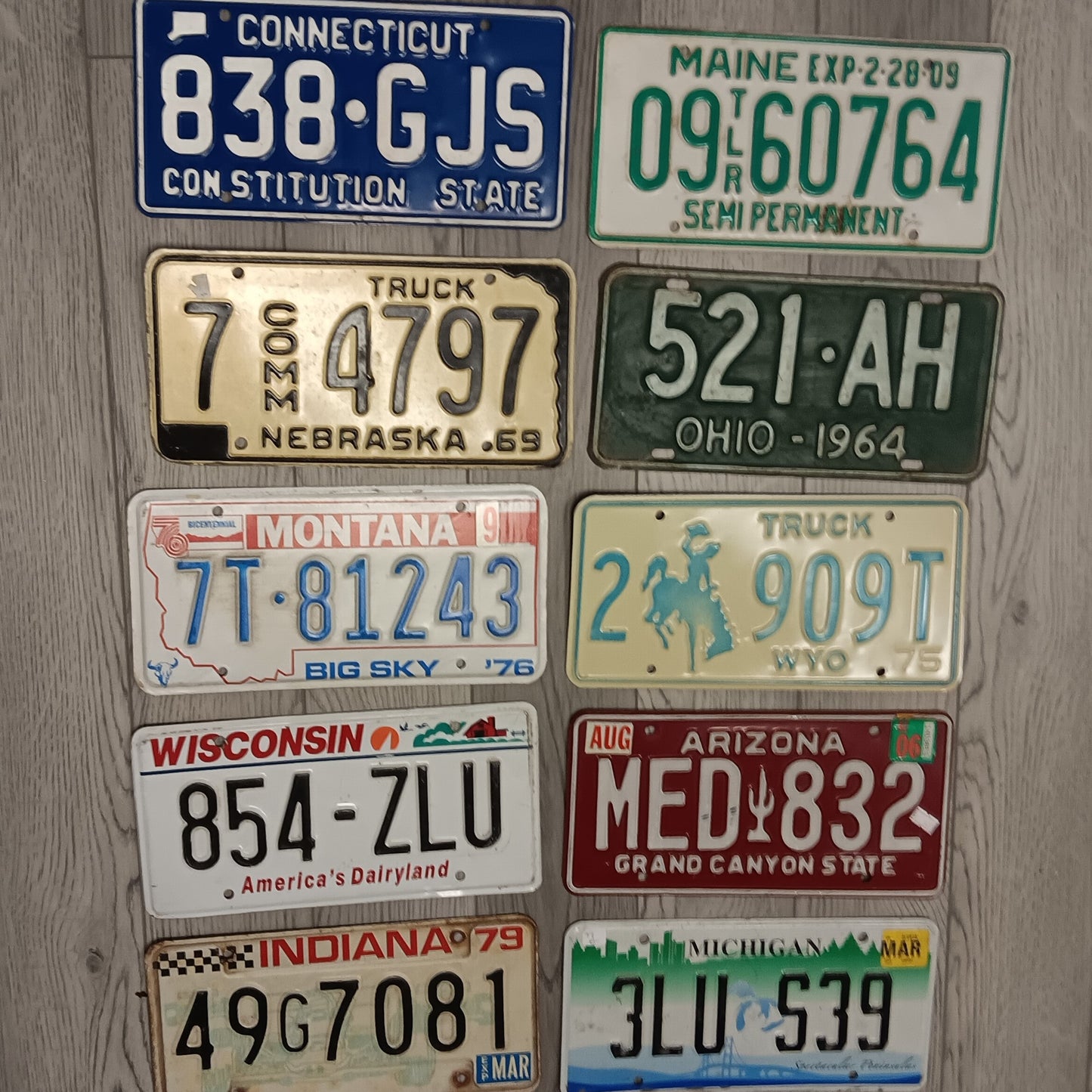 Authentic vintage embossed license plates from multiple U.S. states displayed flat showing raised lettering and classic color designs