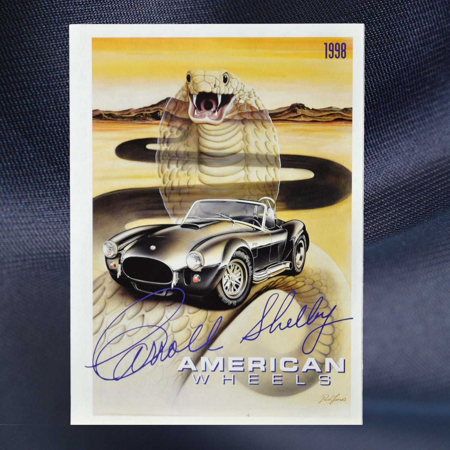 1998 Carroll Shelby American Wheels brochure with Ruel James cover art featuring a Shelby Cobra and dramatic cobra illustration.