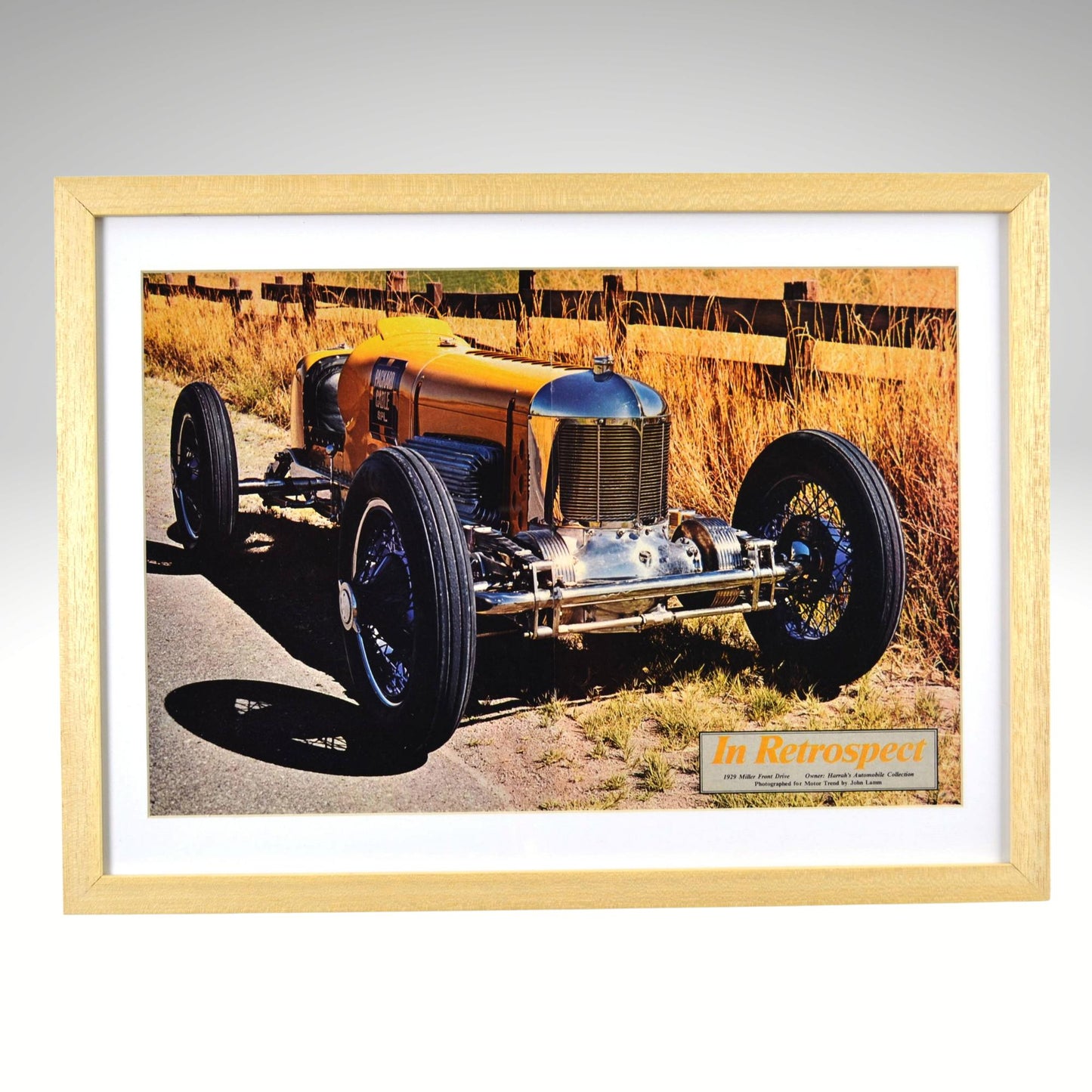 Framed print of a vintage car on a road with a wooden frame.