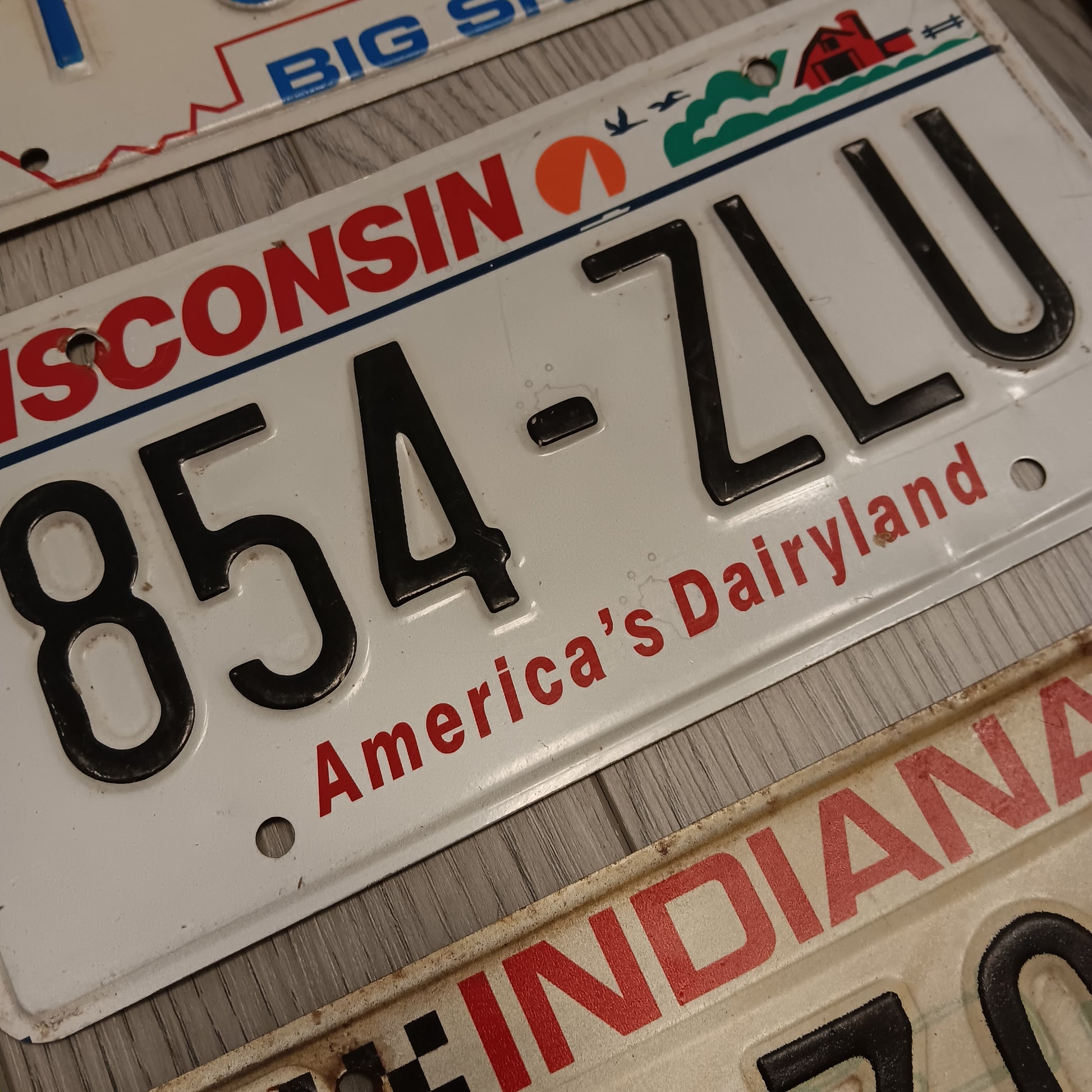 Close up of vintage embossed metal license plates showing raised numbers and authentic road wear from various U.S. states