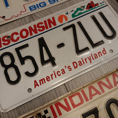 Close up of vintage embossed metal license plates showing raised numbers and authentic road wear from various U.S. states