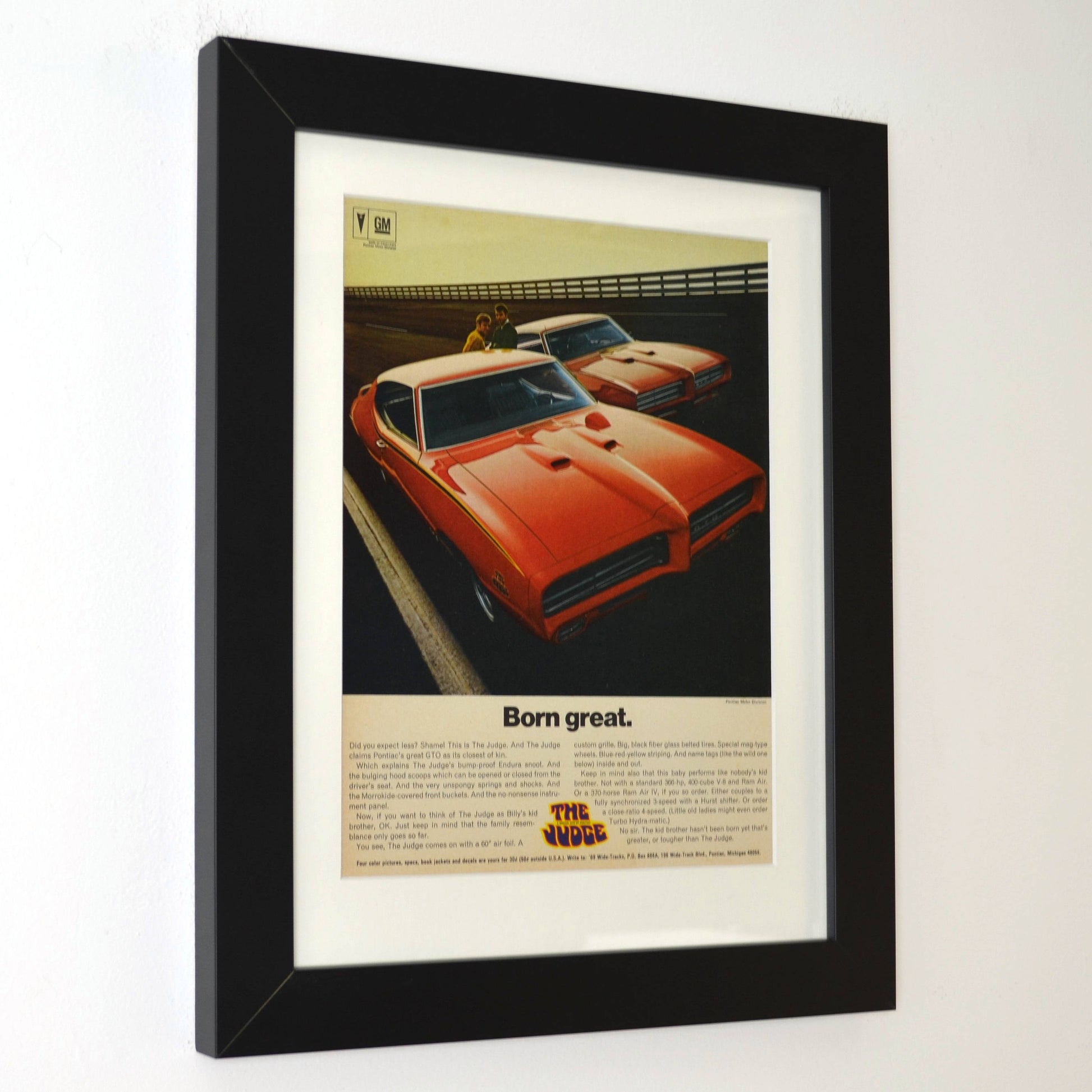 Framed 1969 Pontiac GTO Judge vintage print ad featuring two Carousel Red GTOs with headline “Born Great.” Displayed in a matte black frame with white mat — classic muscle car wall art for collectors and enthusiasts side view