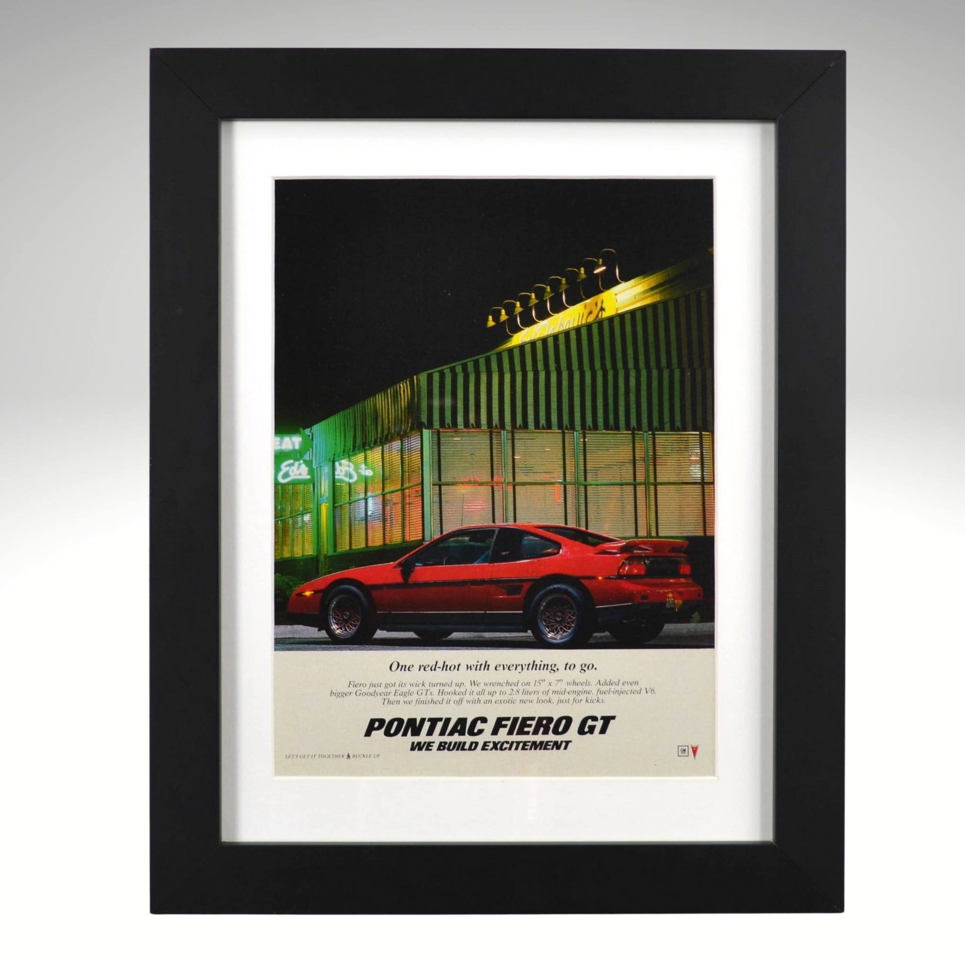 Framed Pontiac Fiero GT ad – red 1980s Fiero parked at neon-lit diner with “One red-hot with everything” tagline.