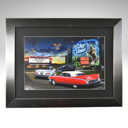 Framed artwork of classic cars in front of a drive-in theater with neon signs.