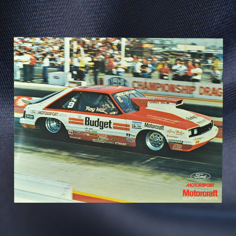 1984 NHRA hero card showing Roy Hill’s Budget-sponsored Mercury Capri Pro Stock car launching down the dragstrip with a crowd in the background.