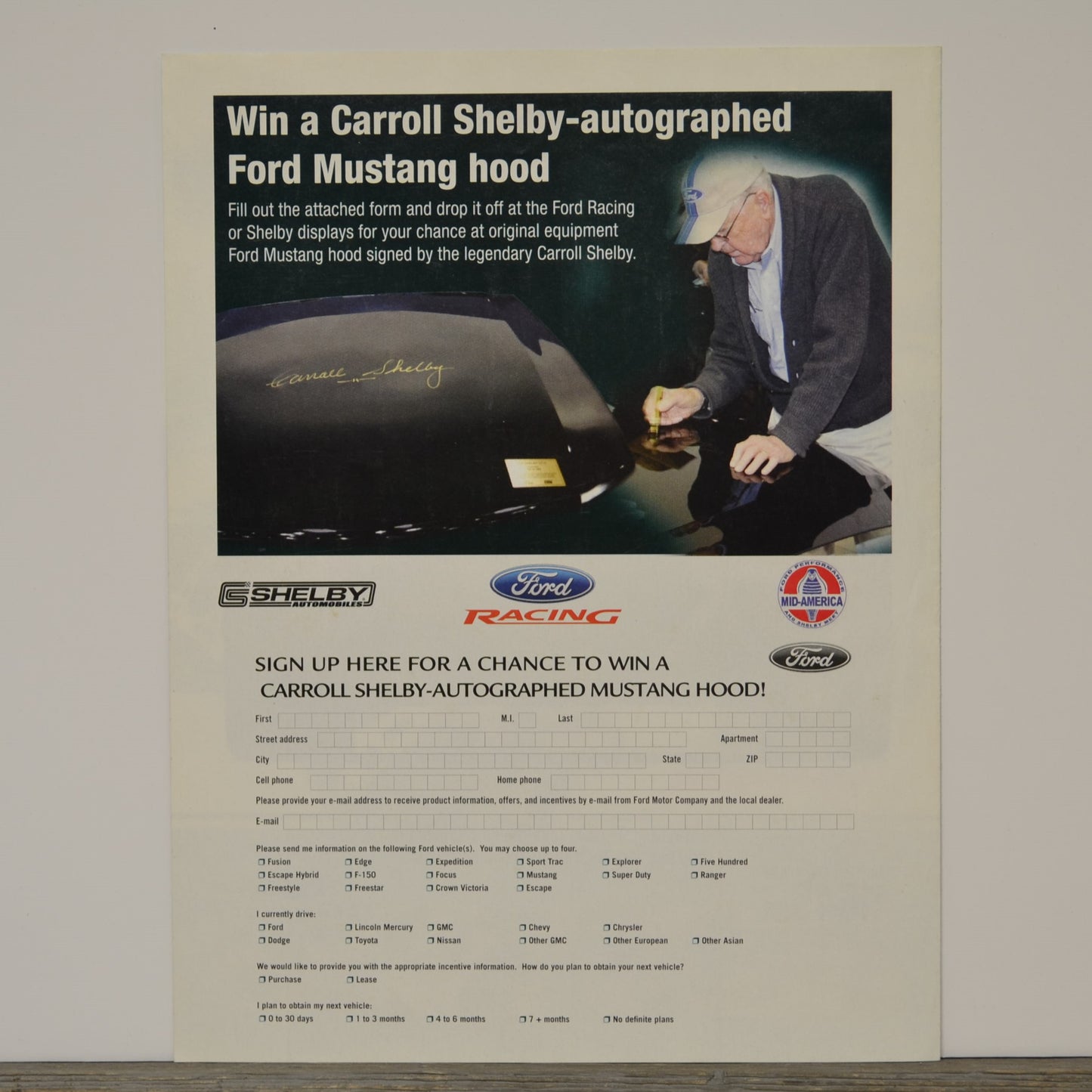 Advertisement for a chance to win a Carroll Shelby-autographed Ford Mustang hood, featuring a man signing the hood.
