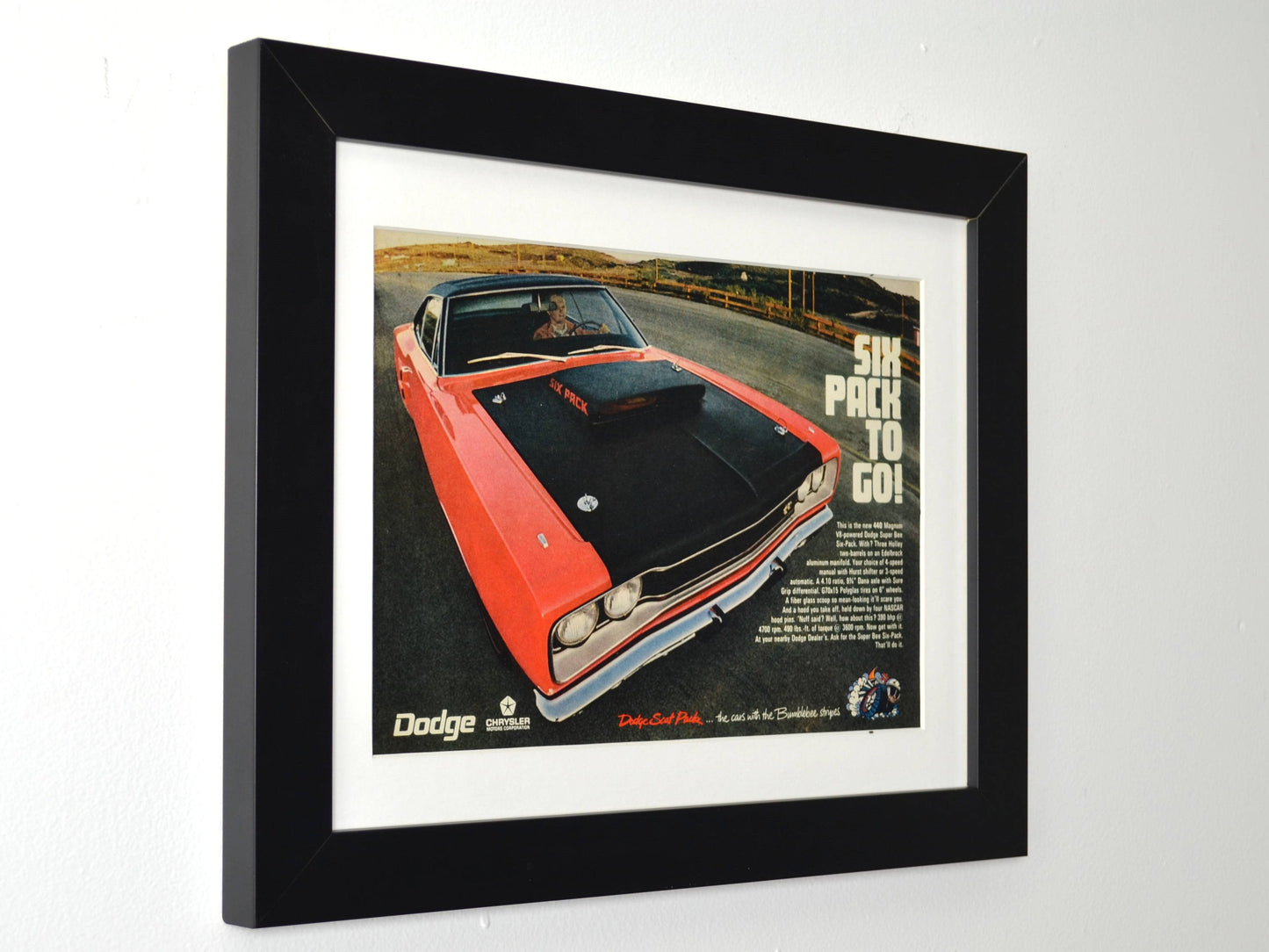 Framed 1970 Dodge Super Bee 440 Six Pack vintage print ad featuring an orange Super Bee with matte black Six Pack hood and “Six Pack to Go!” slogan — authentic Mopar wall art for collectors and enthusiasts side view