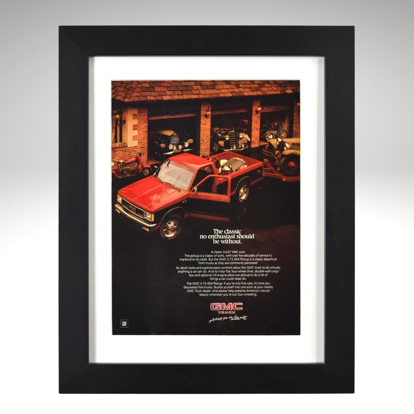 Framed 1980s GMC S-15 pickup truck ad – red compact GMC parked in front of classic cars, vintage framed print for truck collectors.

