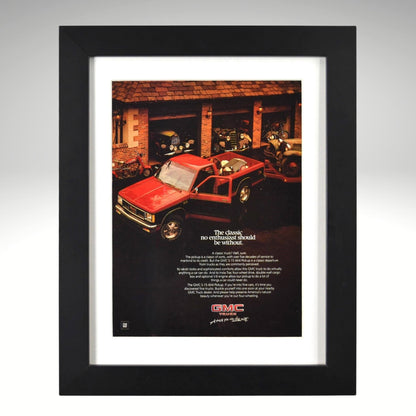 Framed 1980s GMC S-15 pickup truck ad – red compact GMC parked in front of classic cars, vintage framed print for truck collectors.

