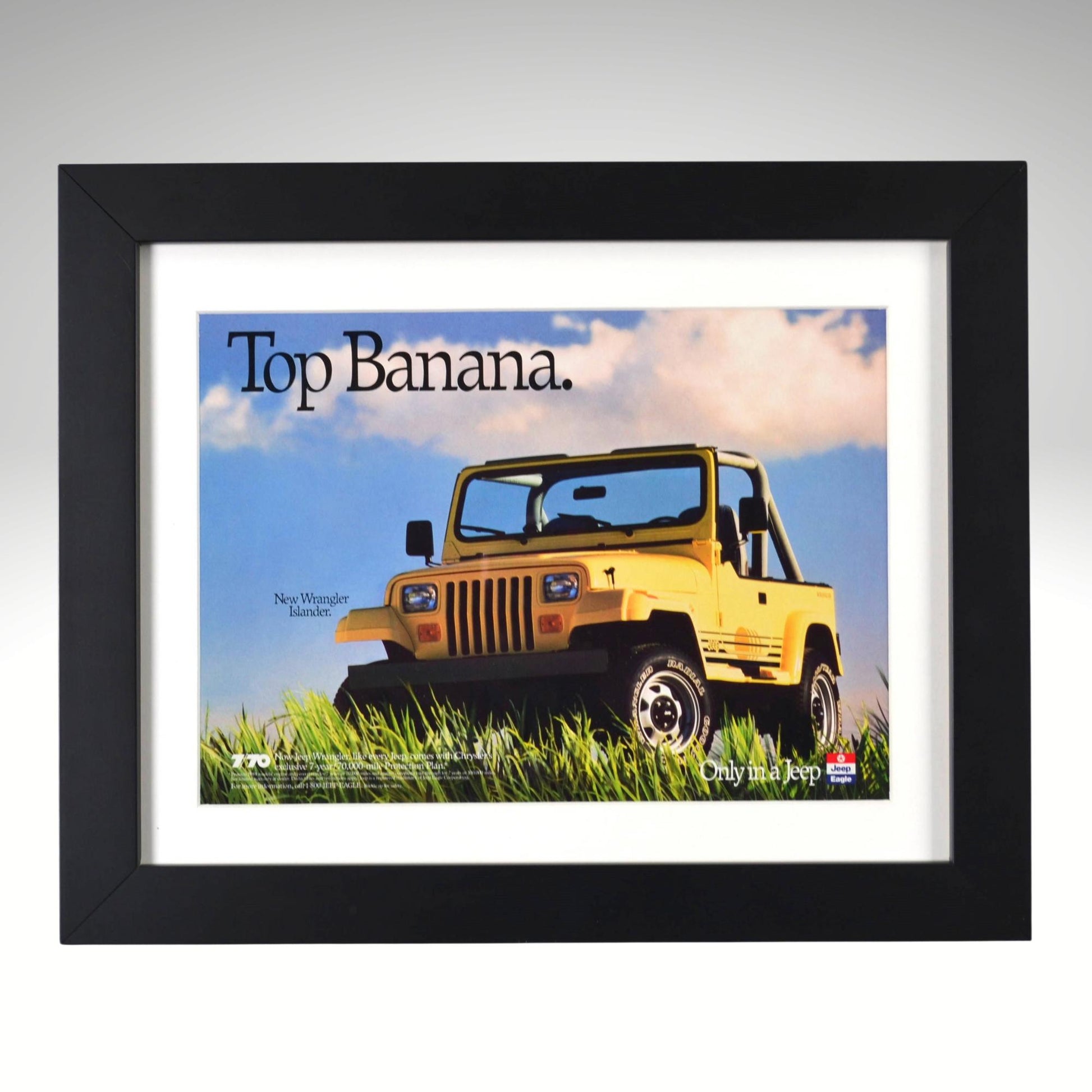 Framed 1989 Jeep Wrangler Islander “Top Banana” vintage print ad featuring yellow Jeep YJ in tall grass with blue sky background.