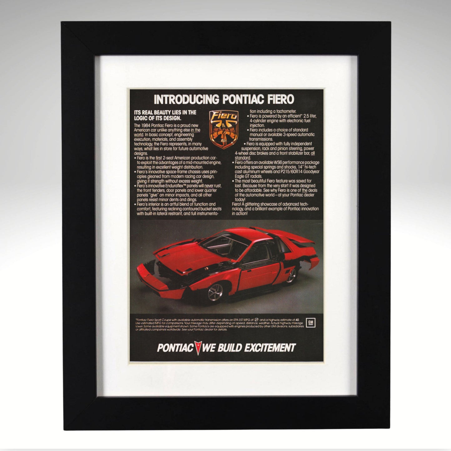 A framed vintage Pontiac Fiero advertisement print, featuring a red sports car and printed text, enclosed in a white mat and a black frame against a light gray background.