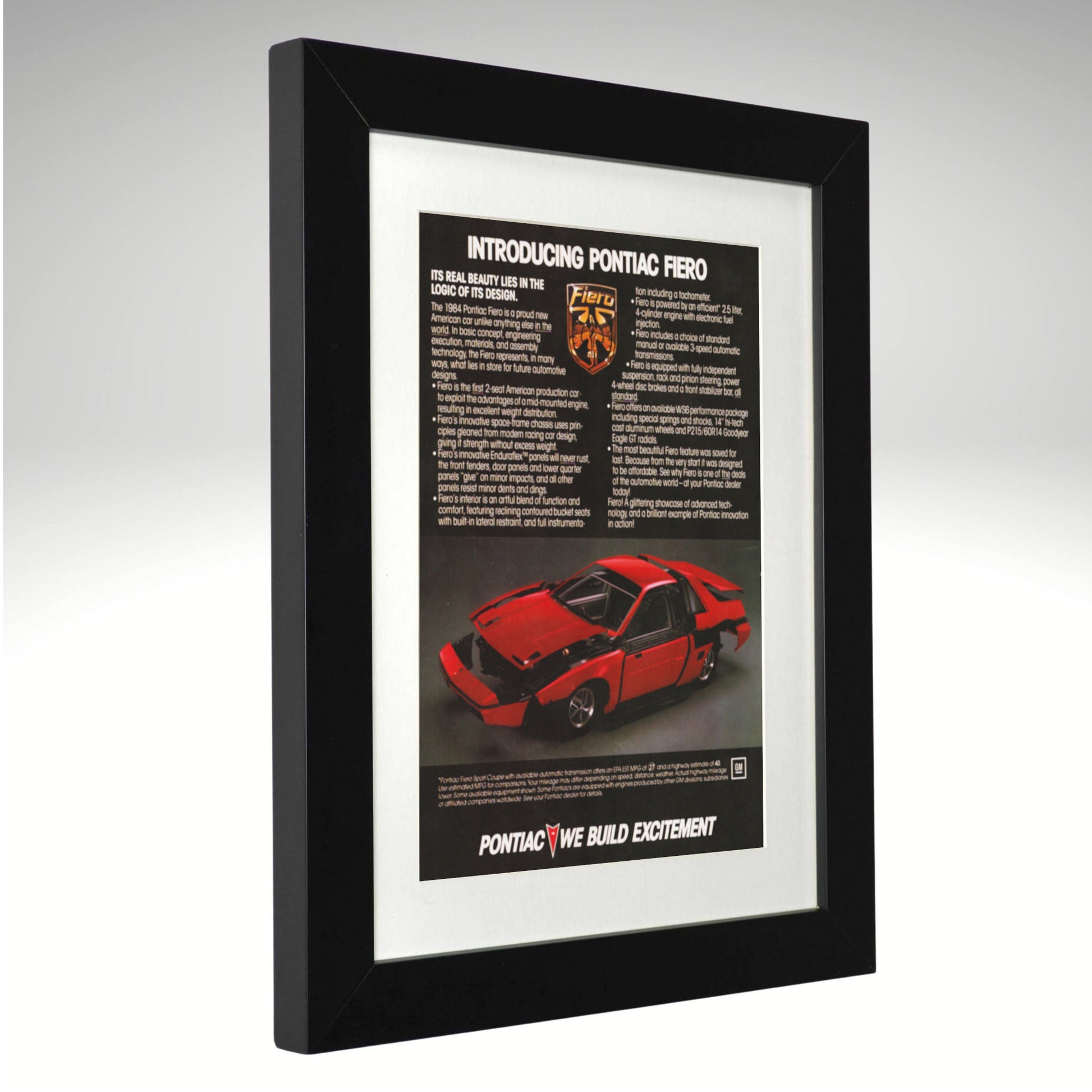 A framed vintage 1984 Pontiac Fiero advertisement print, featuring a black frame, white mat, and a red car graphic on a light gray gradient background.