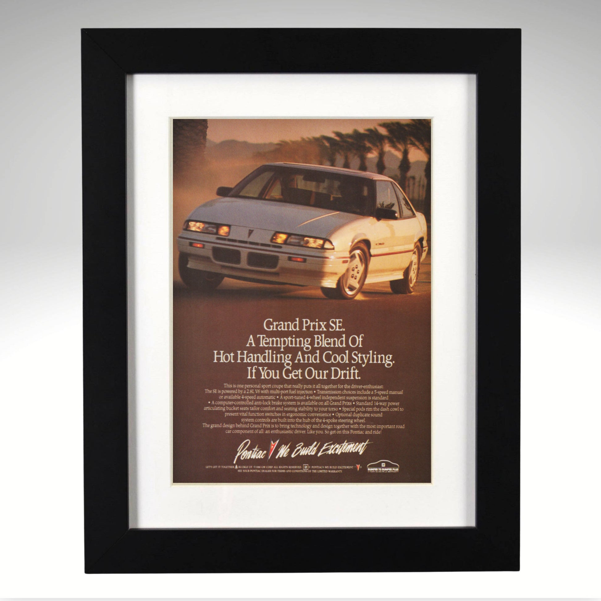 A framed vintage Pontiac Grand Prix SE car advertisement print, featuring a white sports coupe on a desert road with a black frame and white mat.