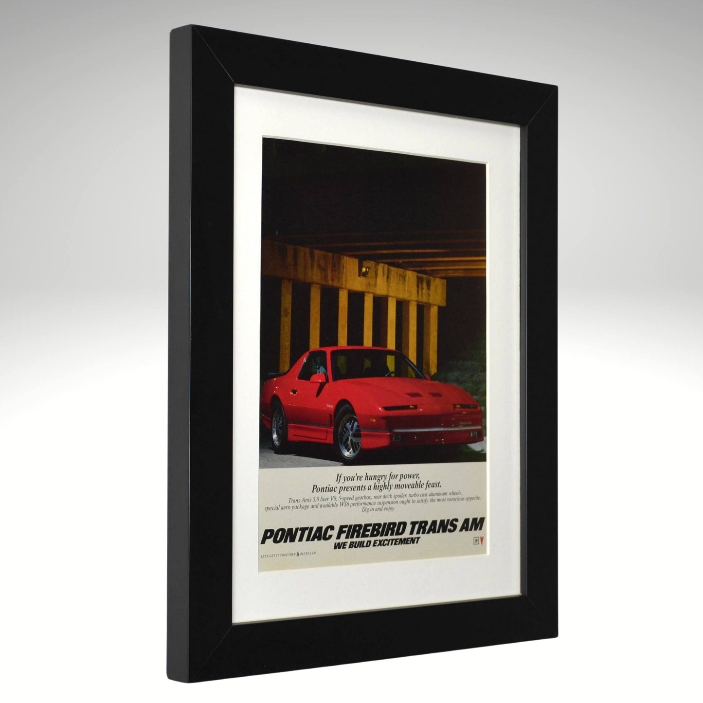 Framed advertisement for Pontiac Firebird Trans Am with a red car on a gray background