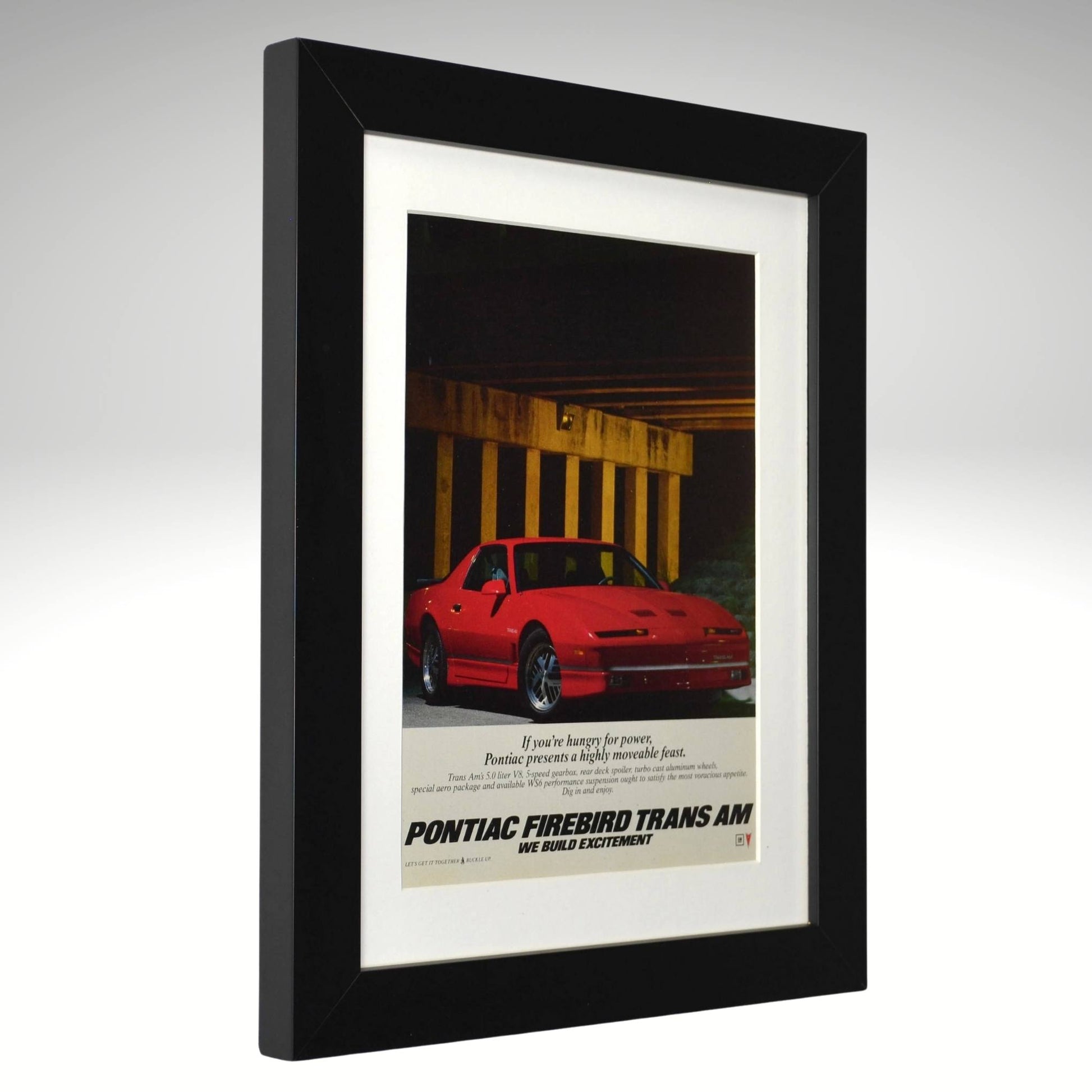 Framed advertisement for Pontiac Firebird Trans Am with a red car on a gray background