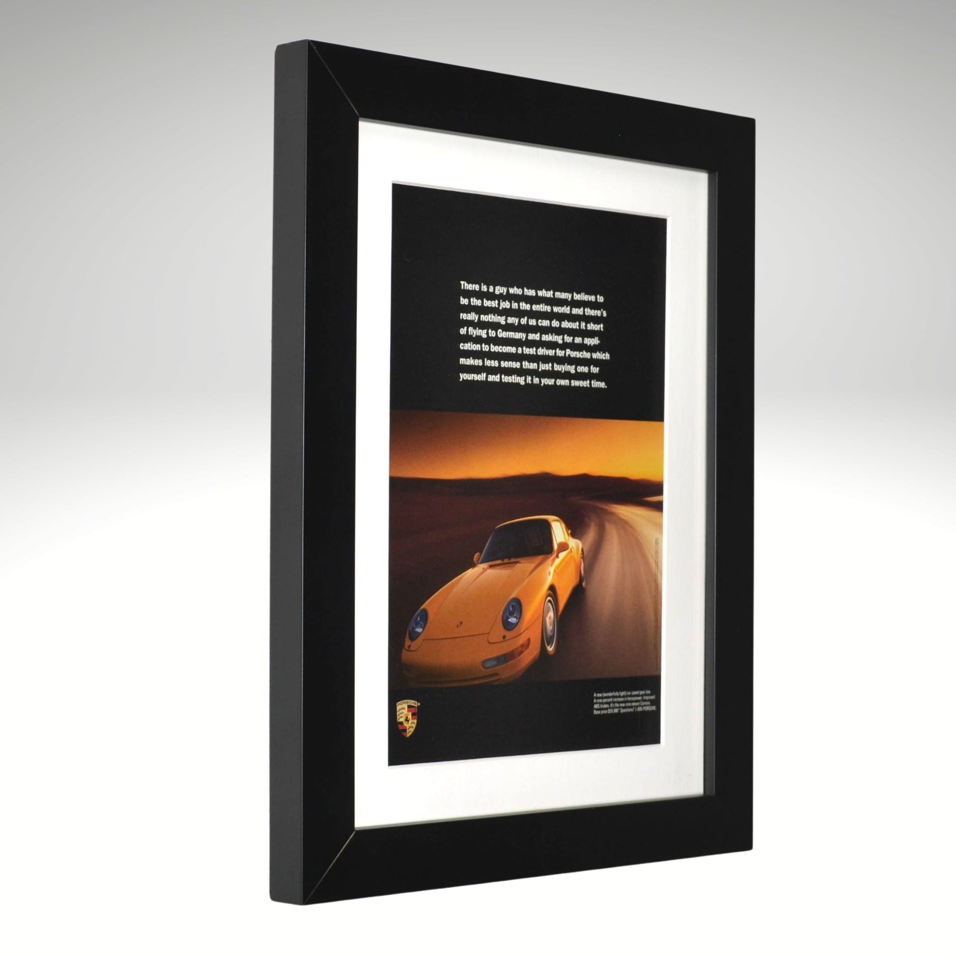 Framed artwork of a yellow Porsche 911 on a desert road with a black background