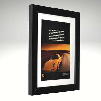 Framed artwork of a yellow Porsche 911 on a desert road with a black background