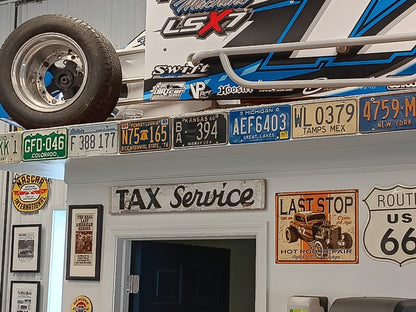 Vintage embossed state license plates mounted as garage wall decor beneath race car shelf in automotive themed workshop